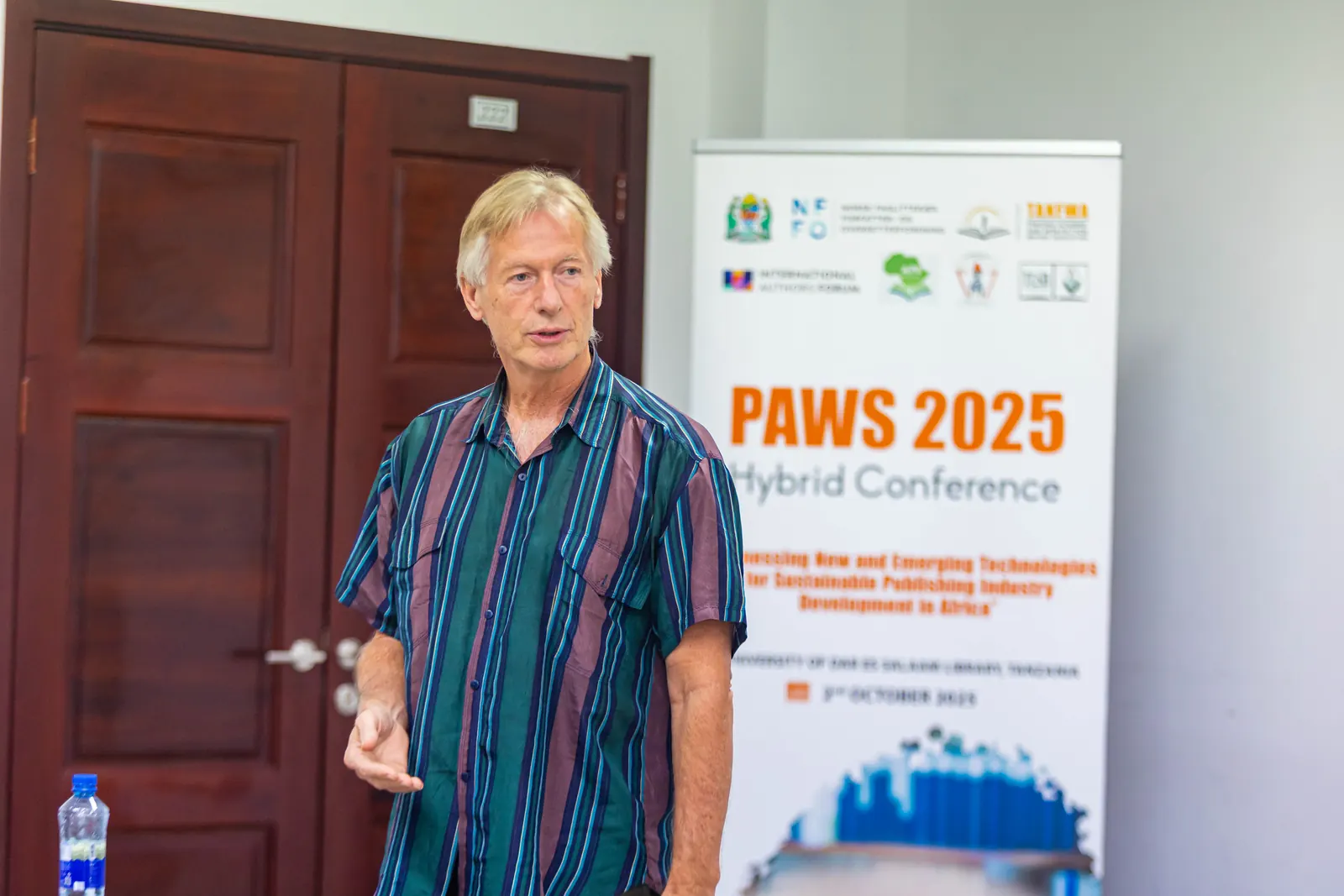 A keynote speaker beside the PAWS 2025 Hybrid Conference banner