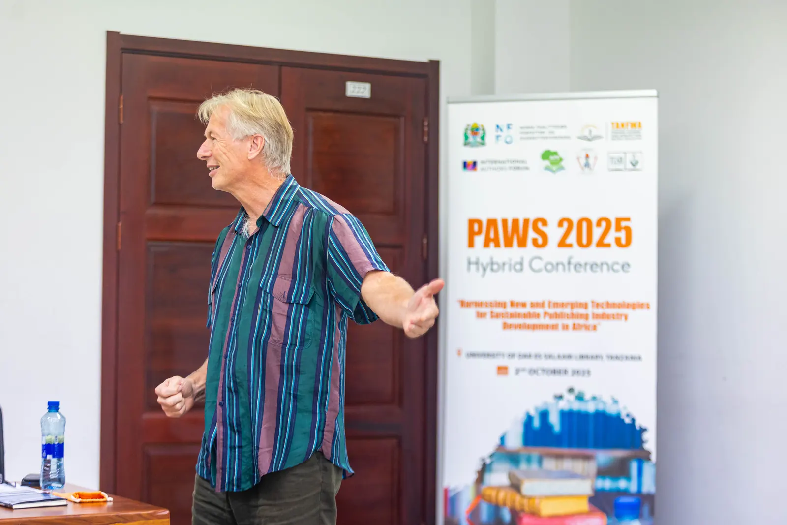 A keynote speaker beside the PAWS 2025 Hybrid Conference banner