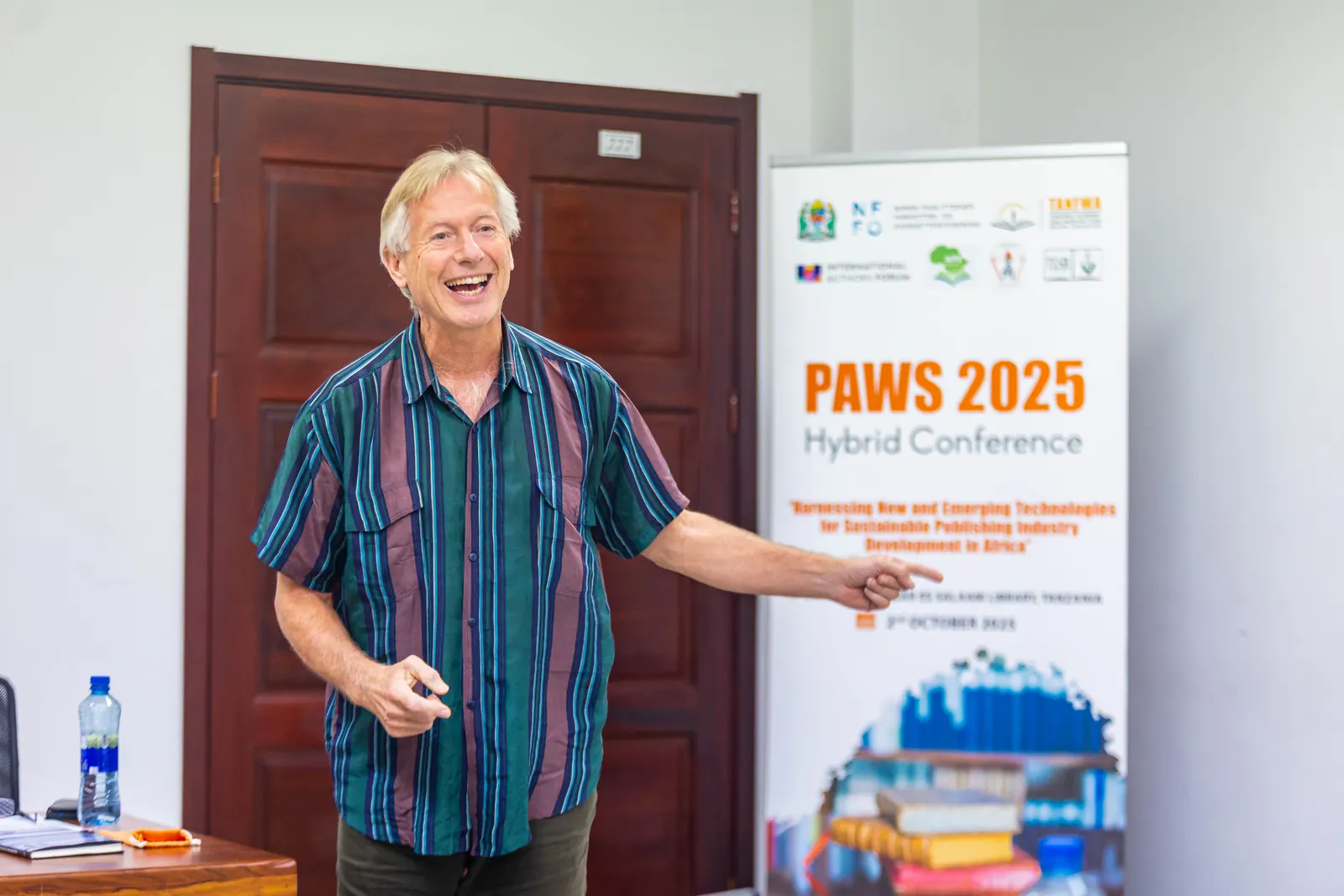 A speaker laughing and pointing at the PAWS 2025 banner