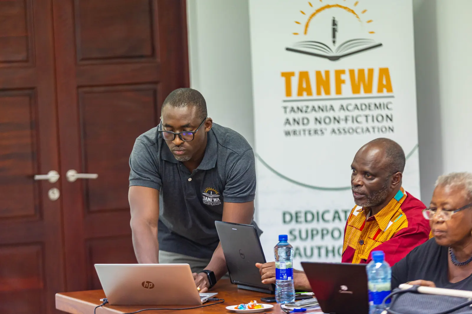 TANFWA team members working together at a laptop beside the TANFWA banner