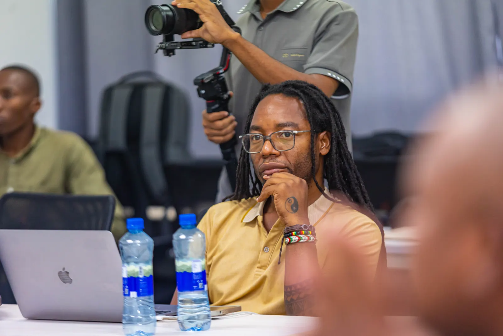 A videographer with a camera on a gimbal filming the session while a delegate listens